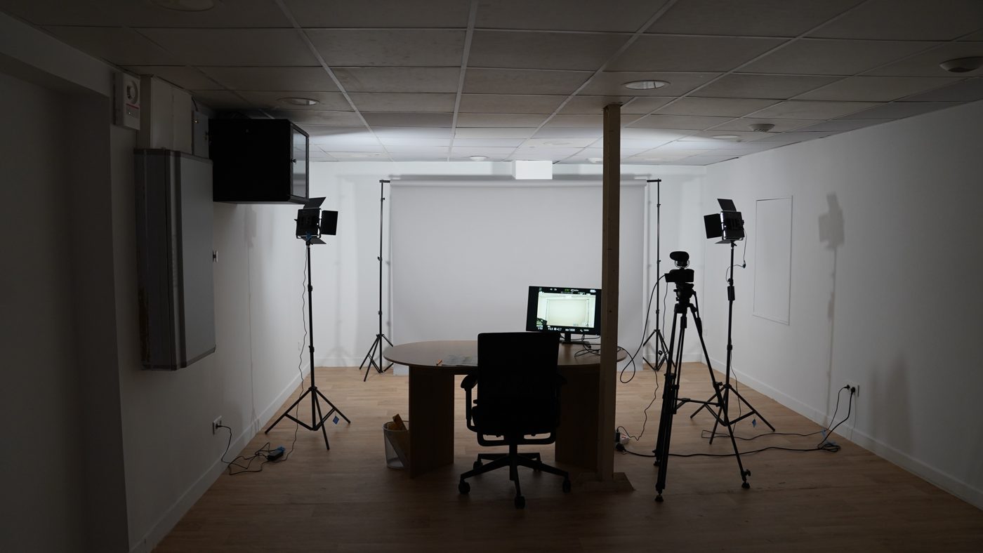 Studio de tournage : fond blanc, bureau et camera